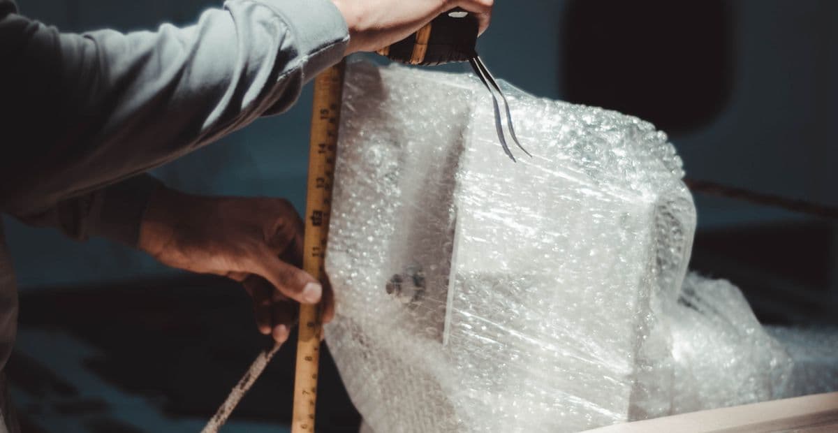 Tangan mengukur tinggi barang yang sudah dibungkus bubble wrap dengan meteran.